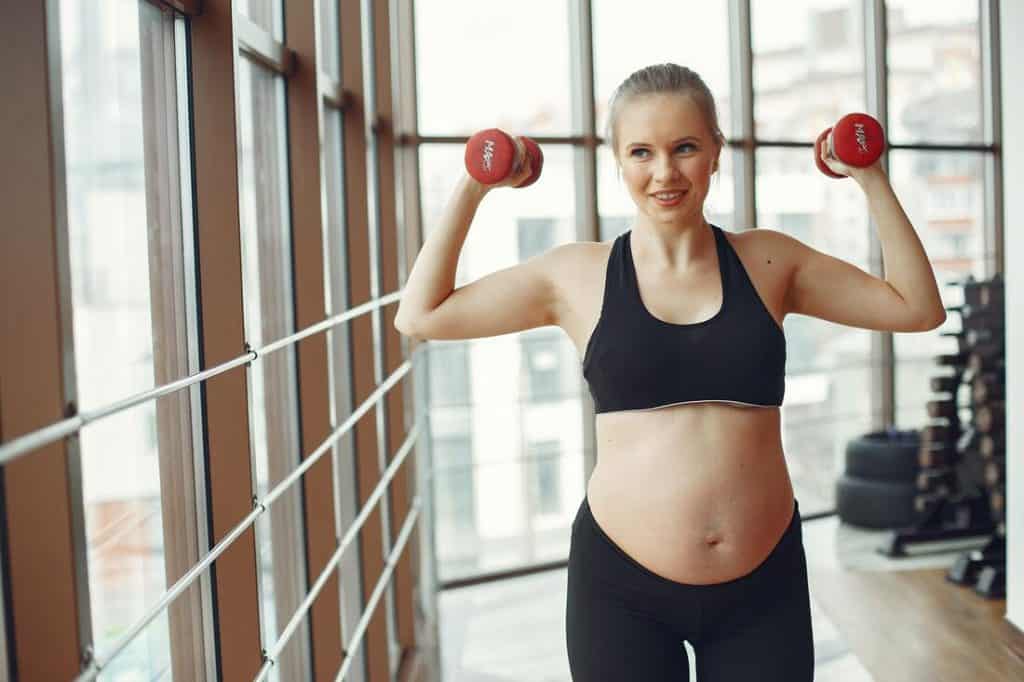 Pregnant woman lifting light dumbbells during workout at gym.