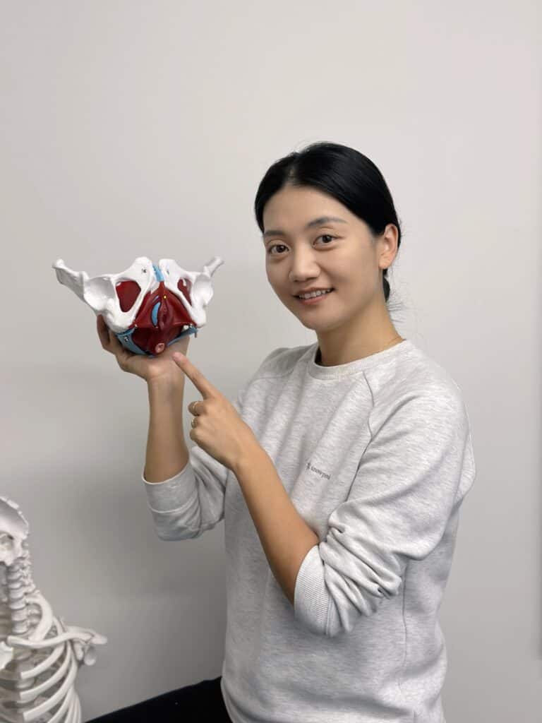 A woman holding a pelvic model demonstrating pelvic health anatomy for physical therapy.