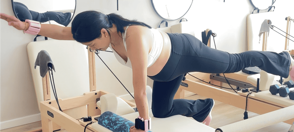 Pregnant woman performing prenatal Pilates exercise on reformer machine at physiotherapy clinic.
